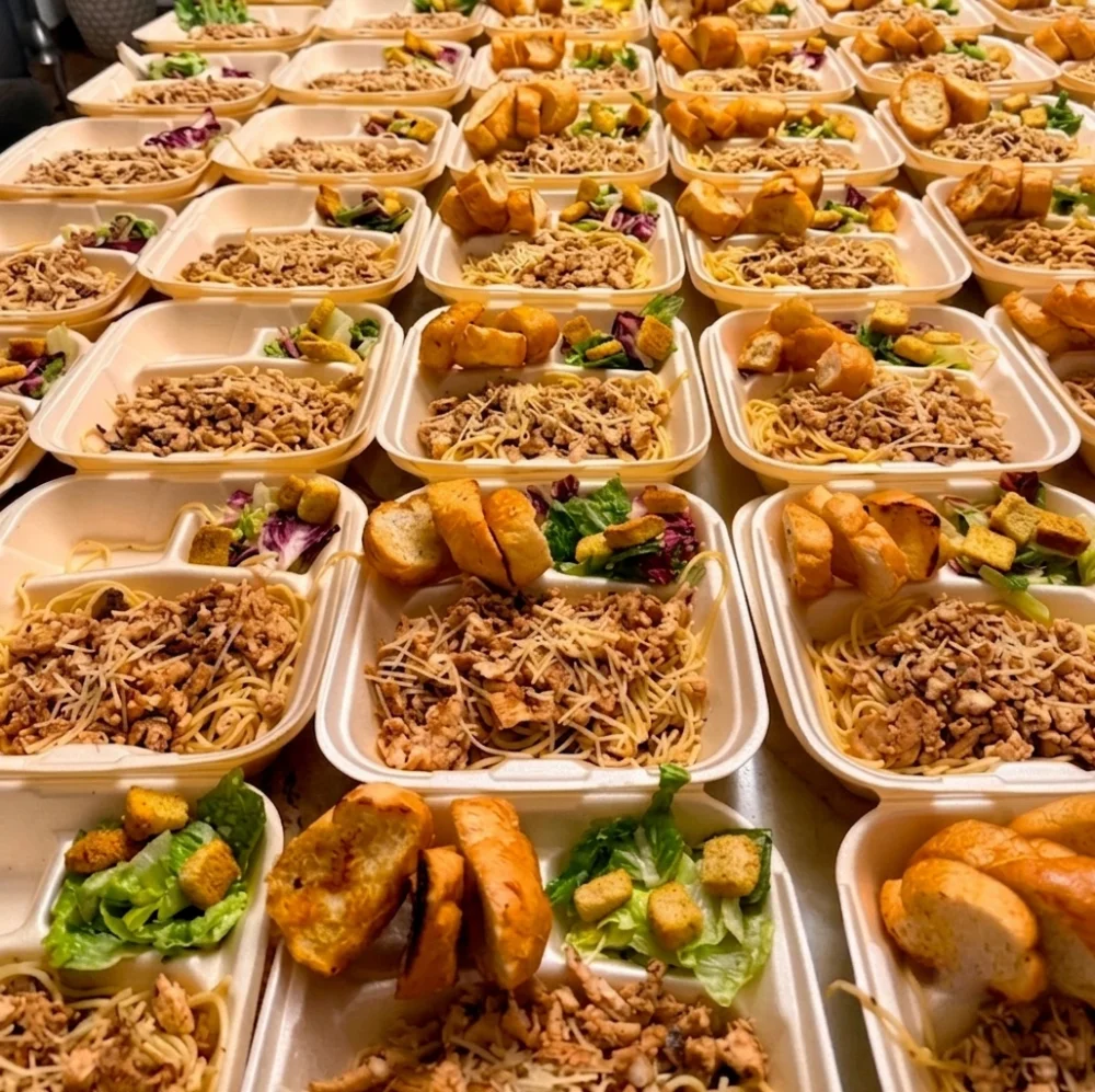 Contenedores de box lunch con pasta, ensalada y pan tostado preparados en volumen para catering de eventos en Salón Palmasola Cancún.