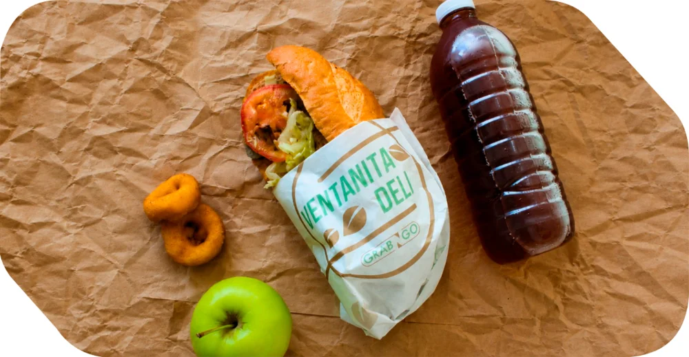 Paquete de box lunch con torta o baguette gourmet, manzana verde y bebida para llevar en eventos corporativos de Salón Palmasola Cancún.
